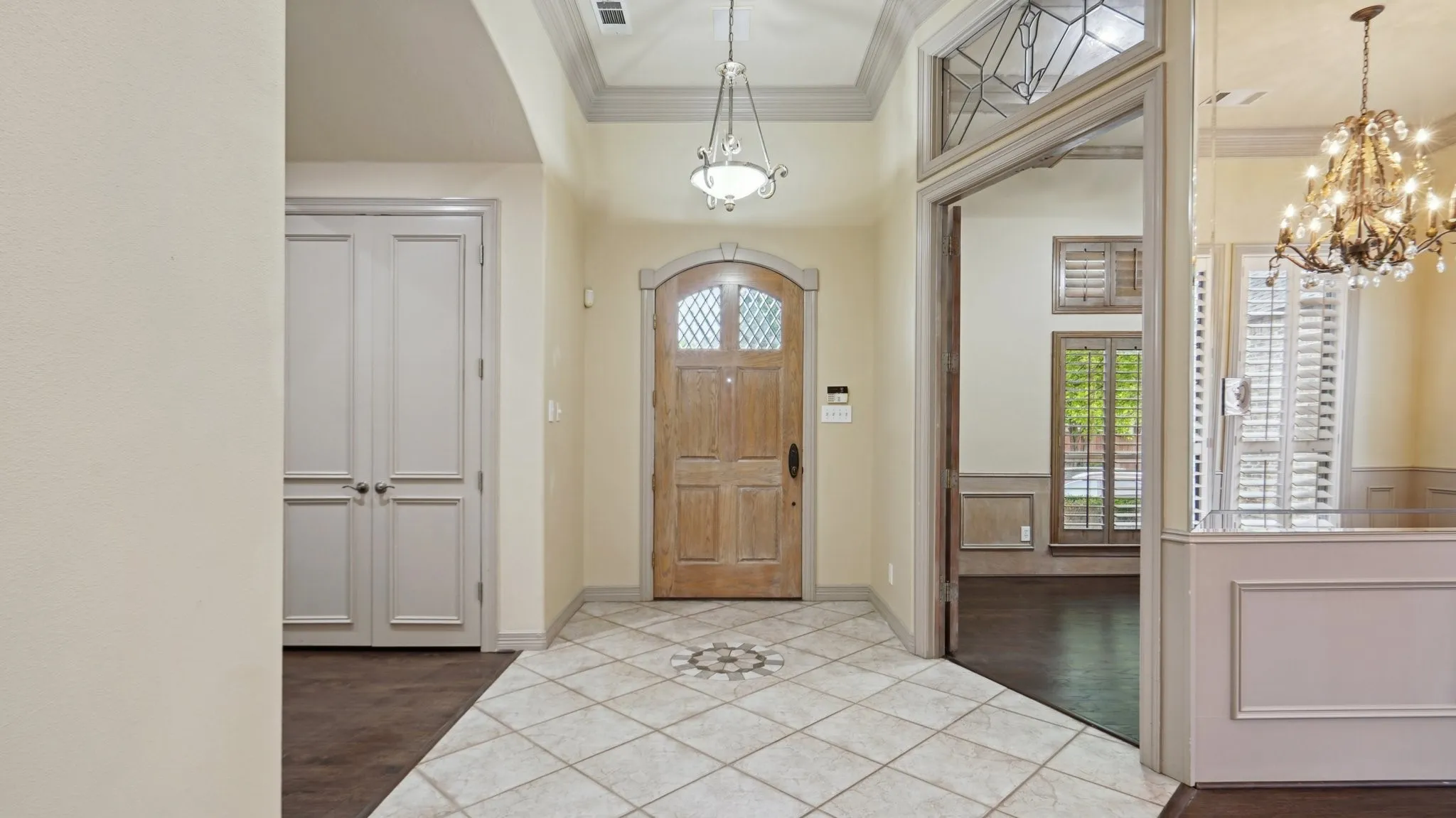 Tiled foyer with crown molding, baseboards, visible vents, and a notable chandelier