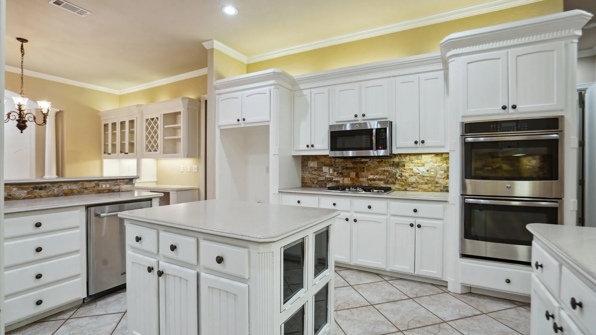 Kitchen featuring visible vents, decorative backsplash, appliances with stainless steel finishes, and glass insert cabinets