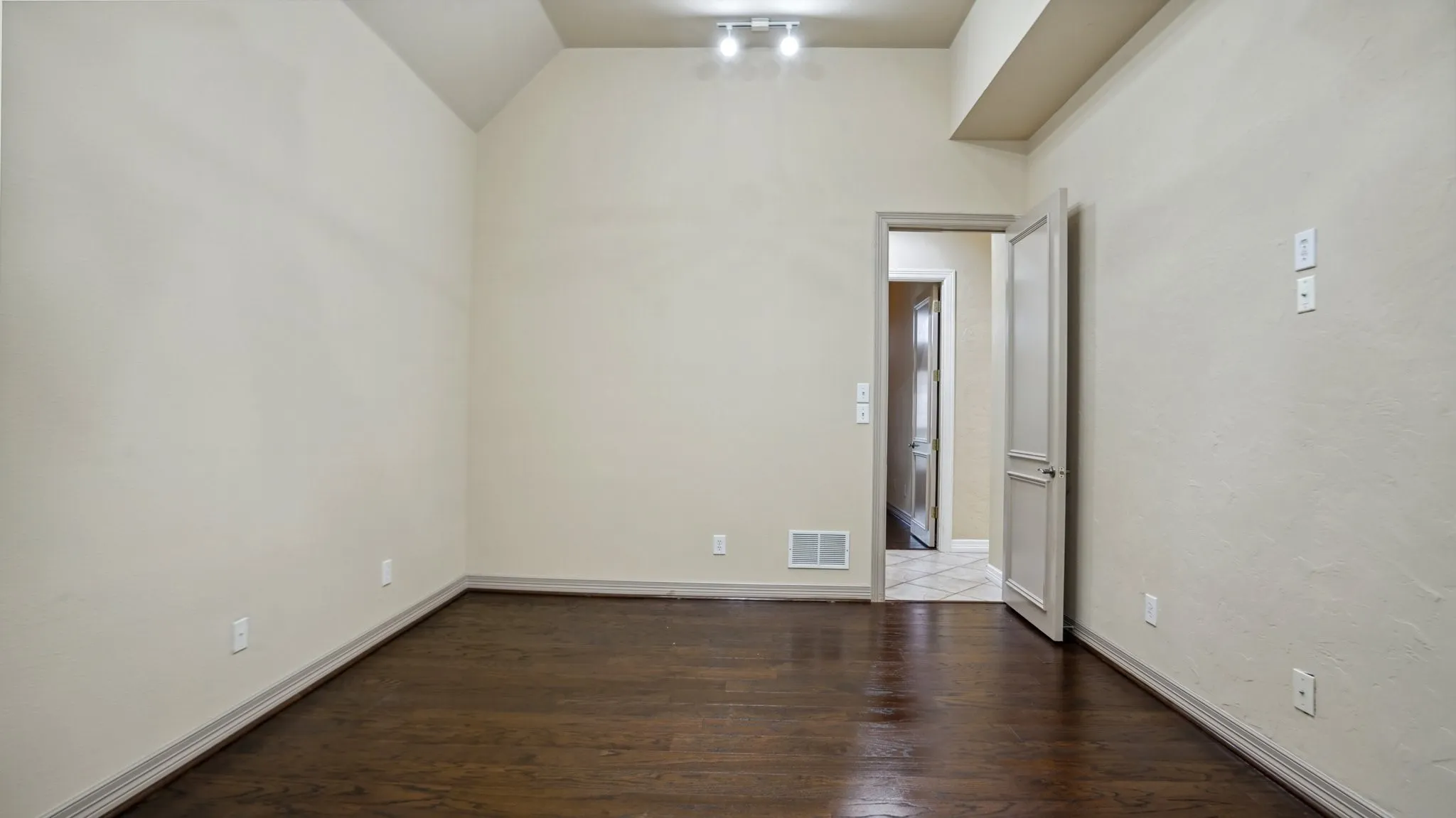 Empty room with visible vents, baseboards, wood finished floors, and vaulted ceiling