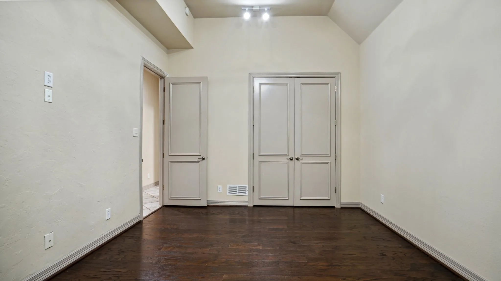 Spare room featuring visible vents, baseboards, dark wood-style flooring, and lofted ceiling