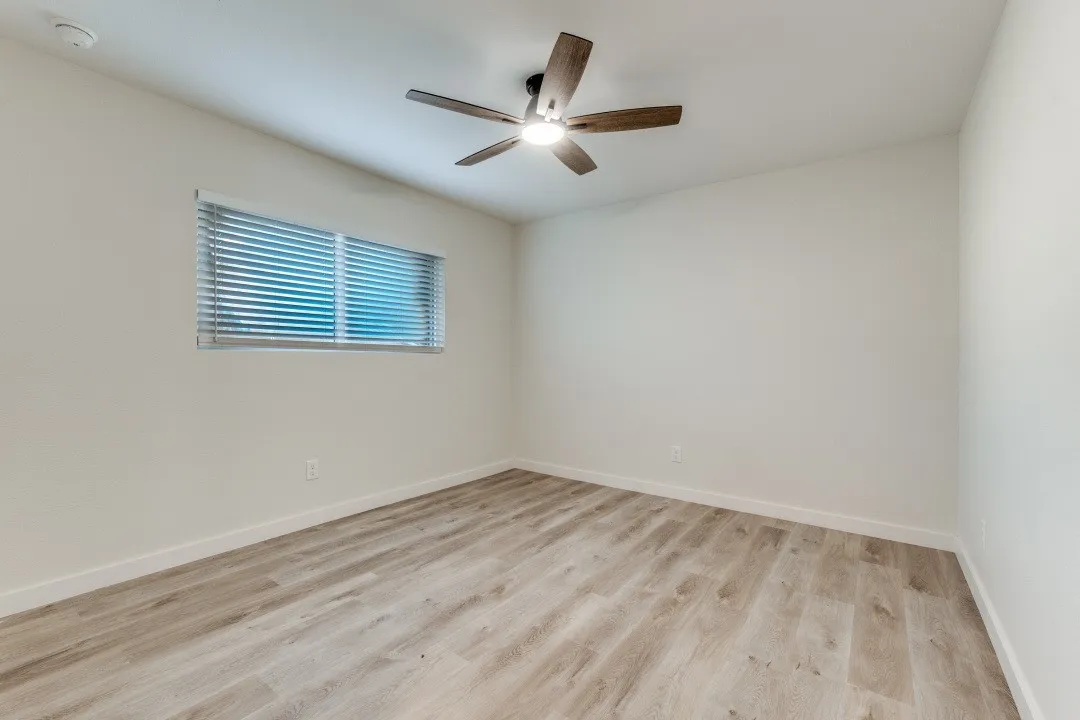 Wood-finish flooring, single window with blinds, ceiling fan with light fixture, and white wall finishes