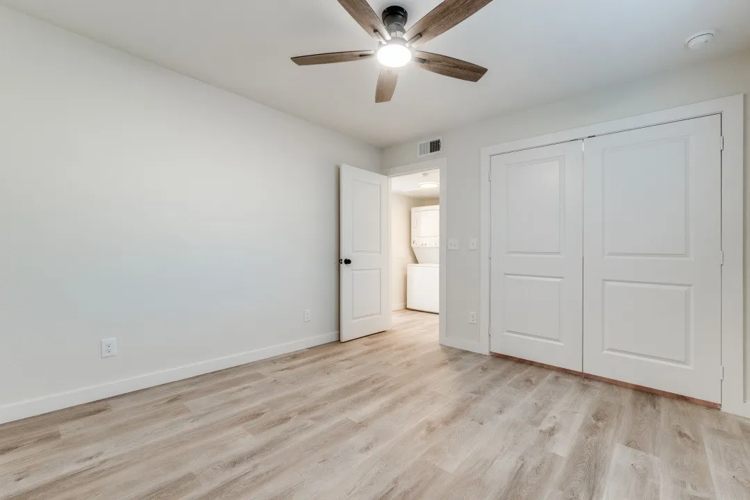 Wood-finish flooring, ceiling fan with integrated lighting, white walls, and white bi-fold closet doors