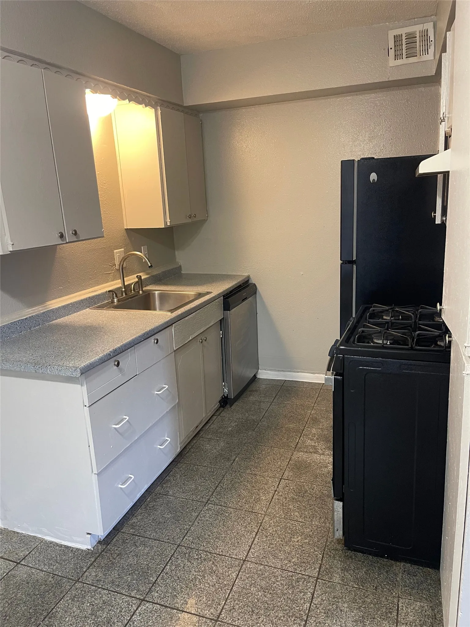 Kitchen featuring tile flooring, a stainless steel sink, a dishwasher, a black refrigerator, and a black range with an oven