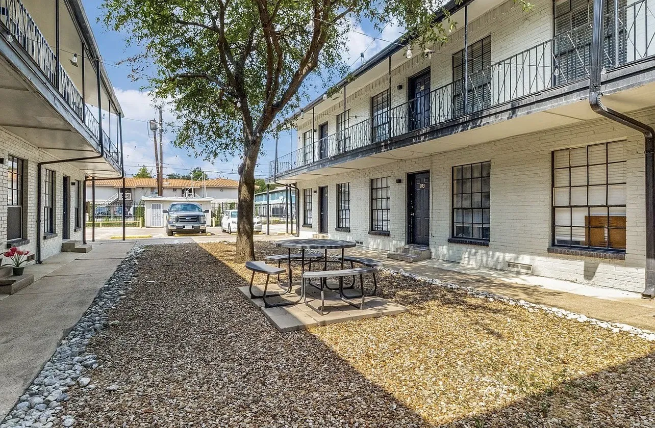 Two-story building featuring white brick facade, black wrought iron railings, black window frames, and a central courtyard