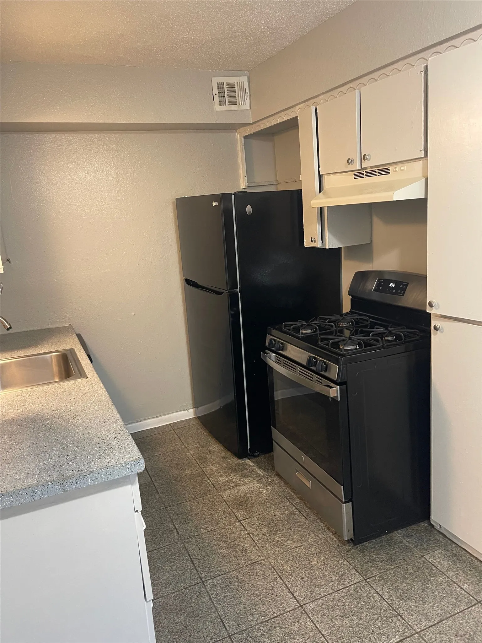 Black refrigerator, stainless steel range, white cabinetry, integrated sink, and tile flooring