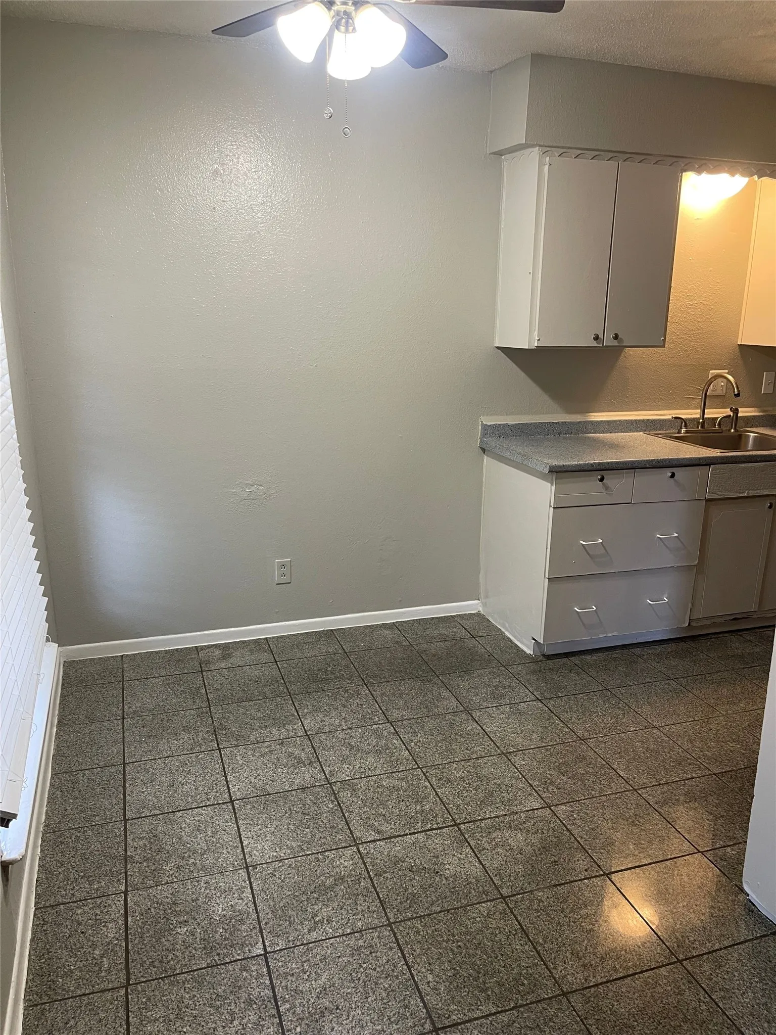 Kitchen space featuring square tile flooring, white cabinetry, a stainless steel sink, and a ceiling fan with integrated lighting