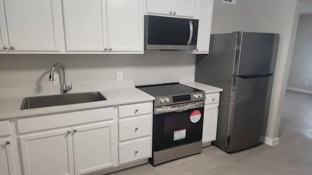 White shaker-style cabinetry with brushed nickel hardware, stainless steel sink with gooseneck faucet, light-toned countertops, stainless steel electric range, and stainless steel refrigerator
