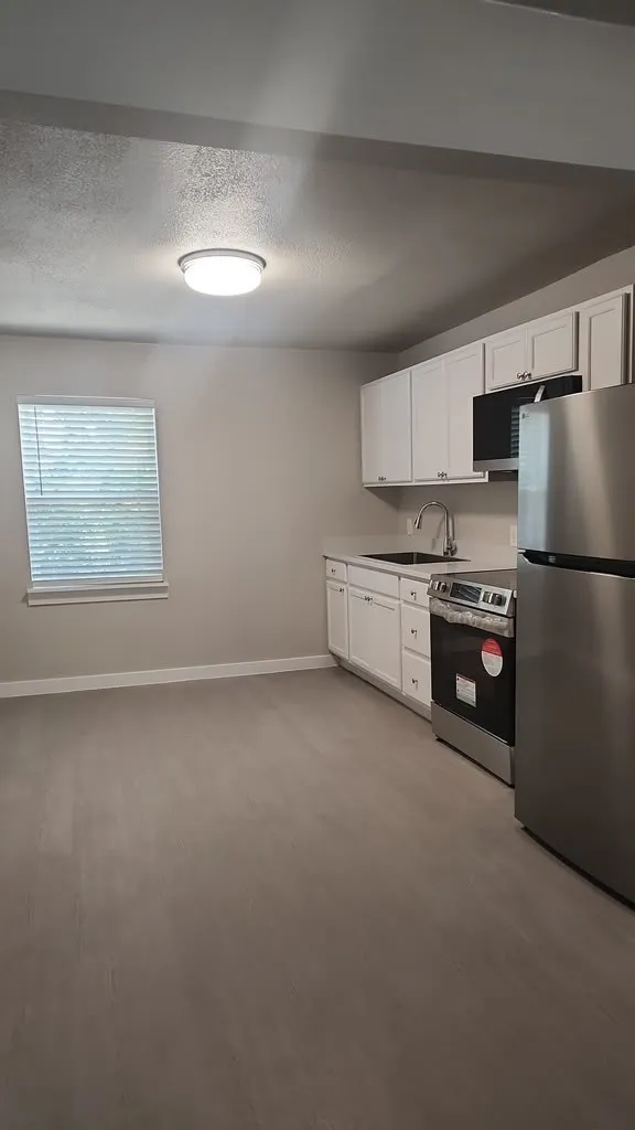 Kitchen area featuring white cabinetry, stainless steel appliances, light gray wood-finish flooring, and a single window with blinds
