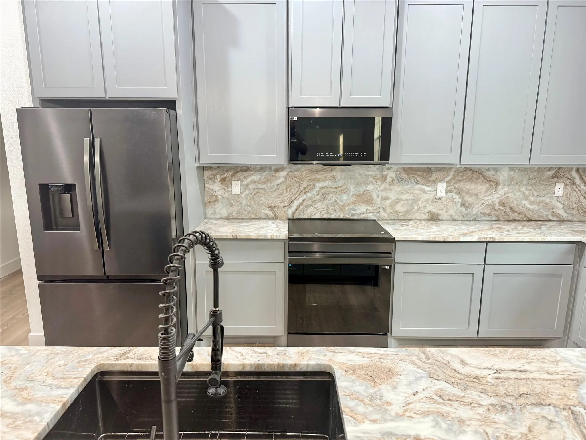 Stainless steel French door refrigerator, black stainless steel dishwasher, over-range microwave, light gray cabinetry, and patterned countertops