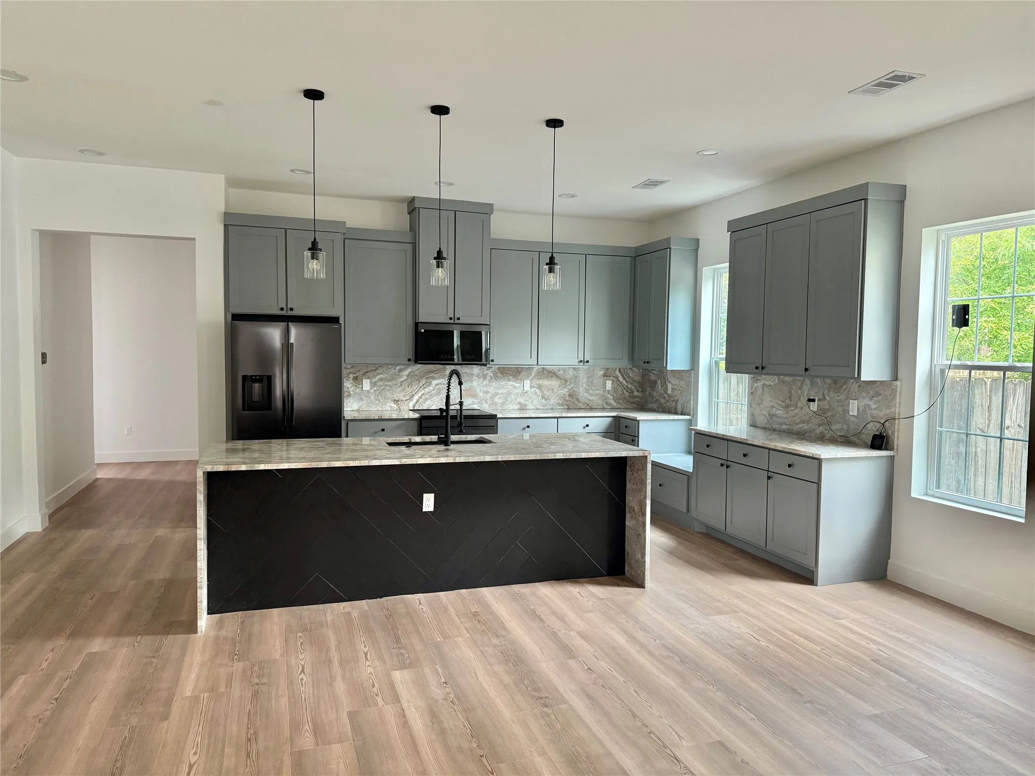 Kitchen featuring light wood-finish flooring, gray cabinetry, integrated appliances, and a central island with a waterfall countertop