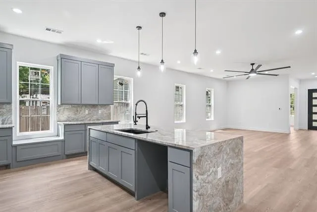 Kitchen island with waterfall countertop, gray cabinetry, black matte faucet, wood-finish flooring, and recessed lighting