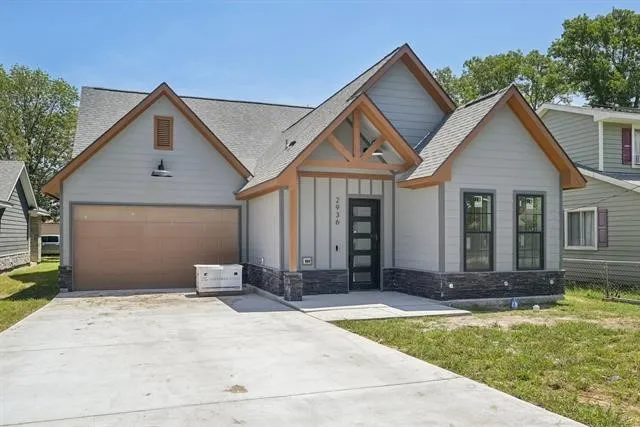 Contemporary exterior featuring gray siding, stone veneer accents, wood-finished gables, a two-car garage, and a concrete driveway