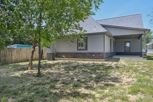 Exterior featuring a covered patio, stacked stone facade accents, light-colored siding, and a fenced perimeter