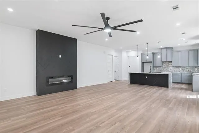 Open-concept living space featuring wood-finish flooring, a contemporary fireplace, recessed lighting, and a modern ceiling fan