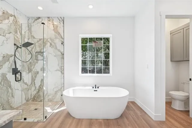 Freestanding soaking tub, walk-in shower with glass enclosure, multi-tone tile shower surround, matte black shower fixtures, and wood-finish flooring