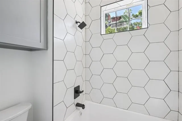 Hexagonal tile shower surround, black-finish shower fixtures, white bathtub, and frosted window