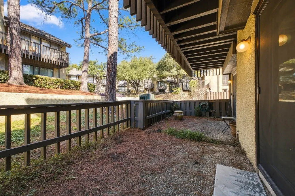 Private patio with a partial fence, overlooking a landscaped berm with mature trees