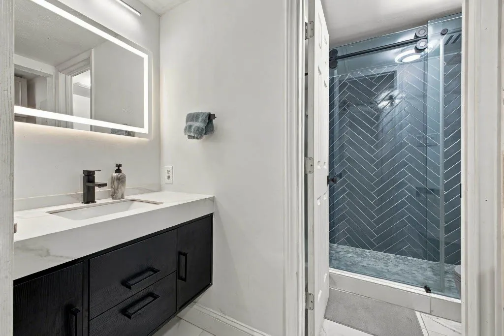 Floating vanity with a white countertop and integrated sink, matte black faucet, and an illuminated mirror