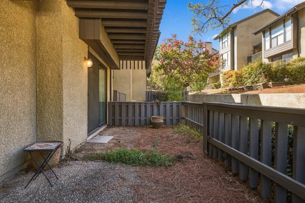 Ground-level patio with a sliding glass door, exterior lighting, and privacy fencing