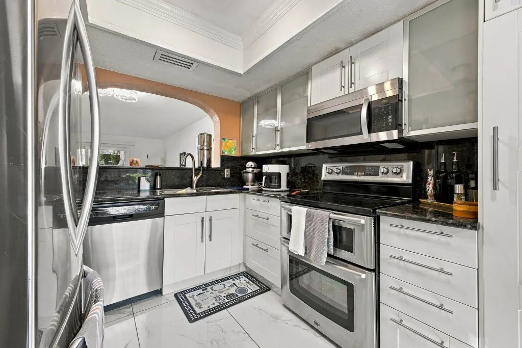 White cabinetry with stainless steel appliances, dark stone countertops, and a full-height dark stone backsplash