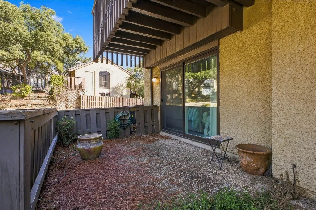 Private outdoor patio with a textured aggregate surface, wood fencing, and a sliding glass door entry