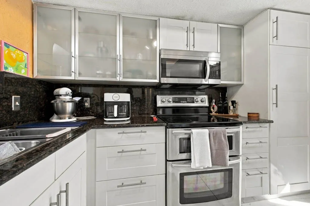 Stainless steel appliances, double oven, built-in microwave, dark stone countertops, and white cabinetry