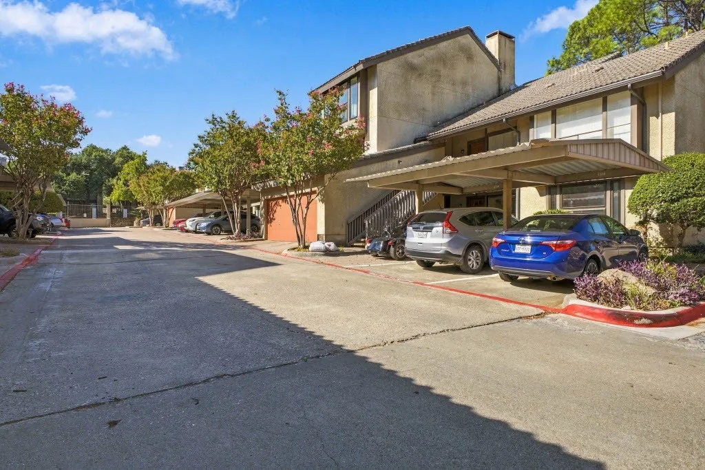 Carport parking beneath a residential structure, featuring mature trees and landscaping