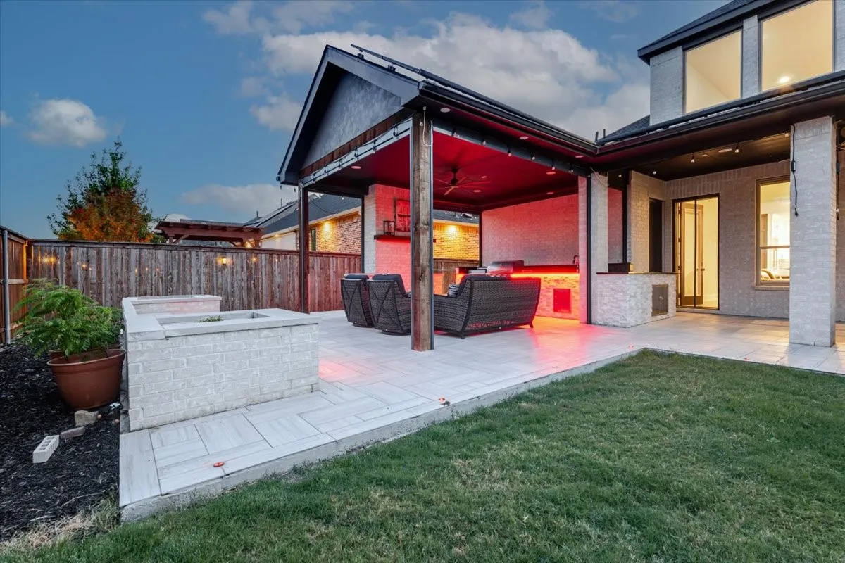 Covered outdoor living area with a stone-clad kitchen, integrated lighting, and ceiling fan
