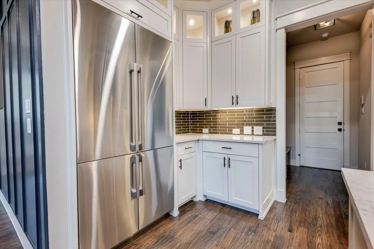 Stainless steel refrigerator, white shaker-style cabinetry, subway tile backsplash, under-cabinet lighting, and wood-finish flooring