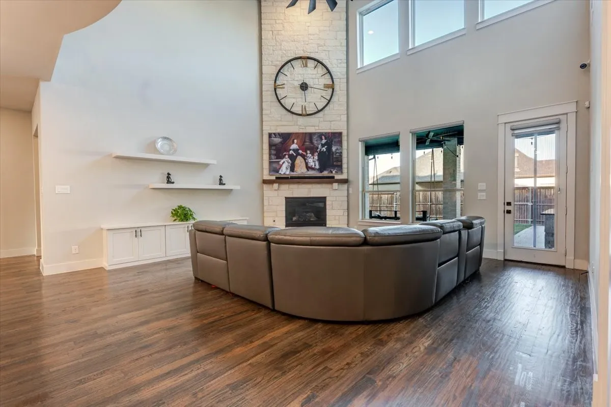 Spacious living area featuring wood-finish flooring, a stone-clad fireplace with a mantel, built-in shelving, and large windows with transom panels