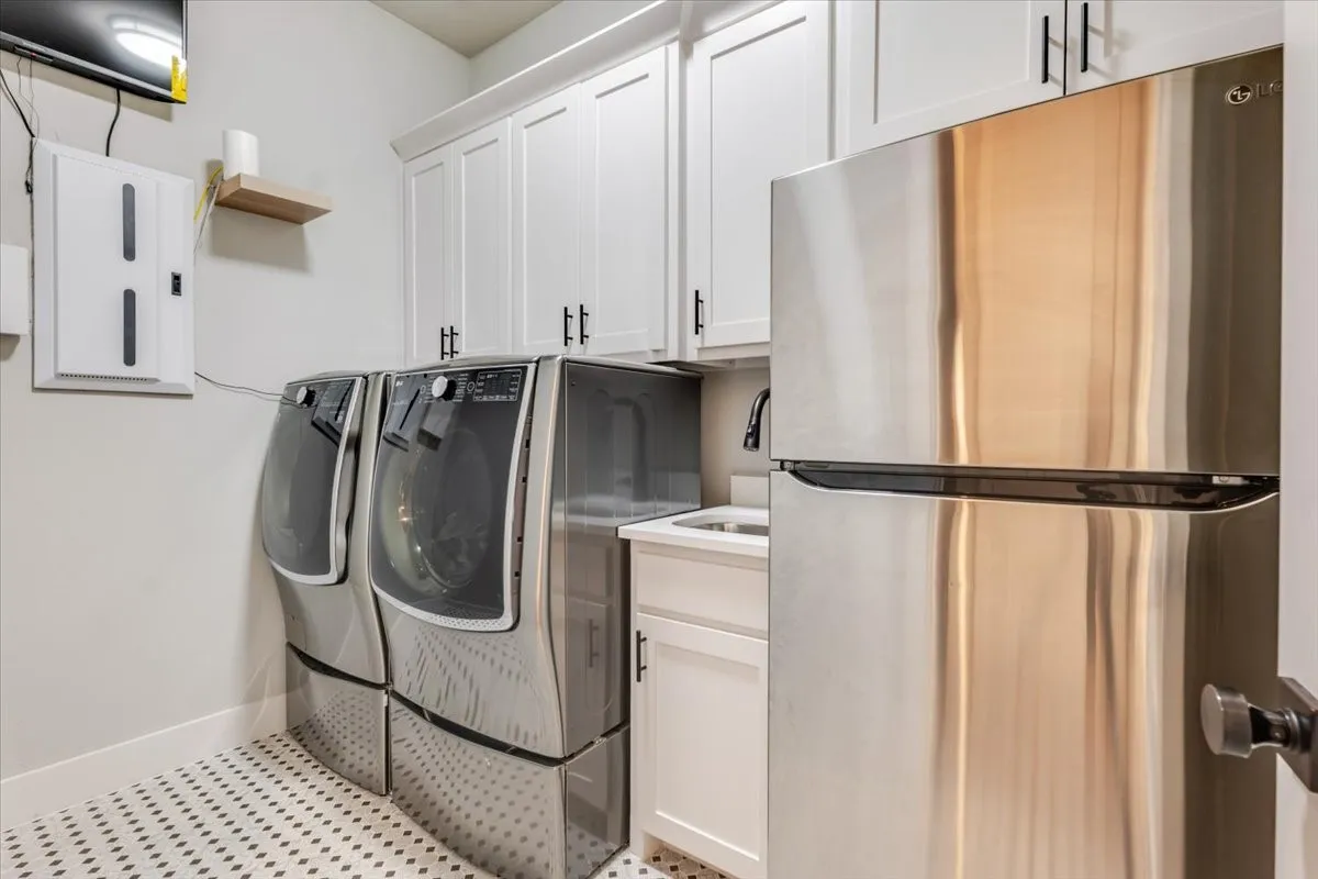 White shaker cabinetry with black hardware, stainless steel appliances, ceramic mosaic tile flooring, and a utility sink