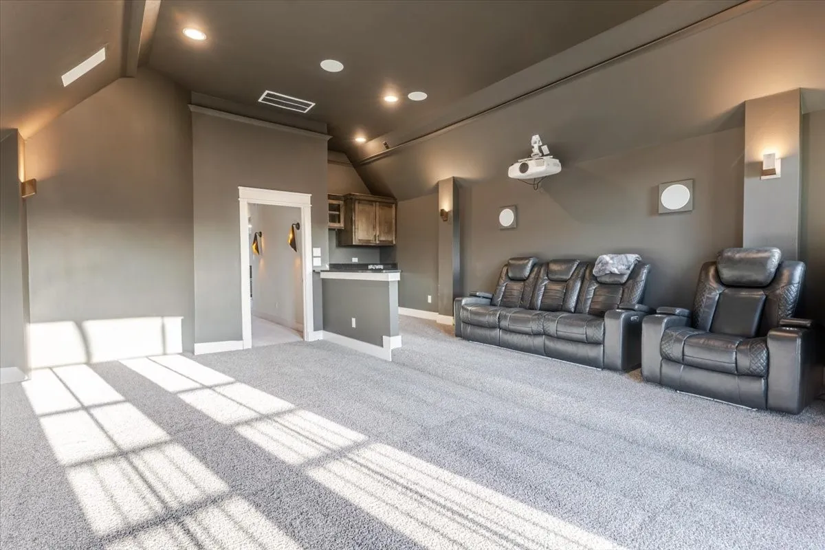 Recessed lighting, built-in projector, wall-mounted sconces, light gray carpeting, and a built-in wet bar with wood-finish cabinetry