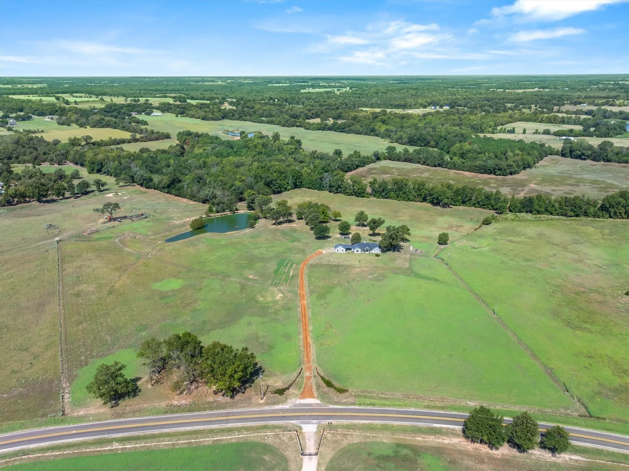 Expansive green acreage featuring a private pond, mature trees, a single-story residence, and a direct road entrance
