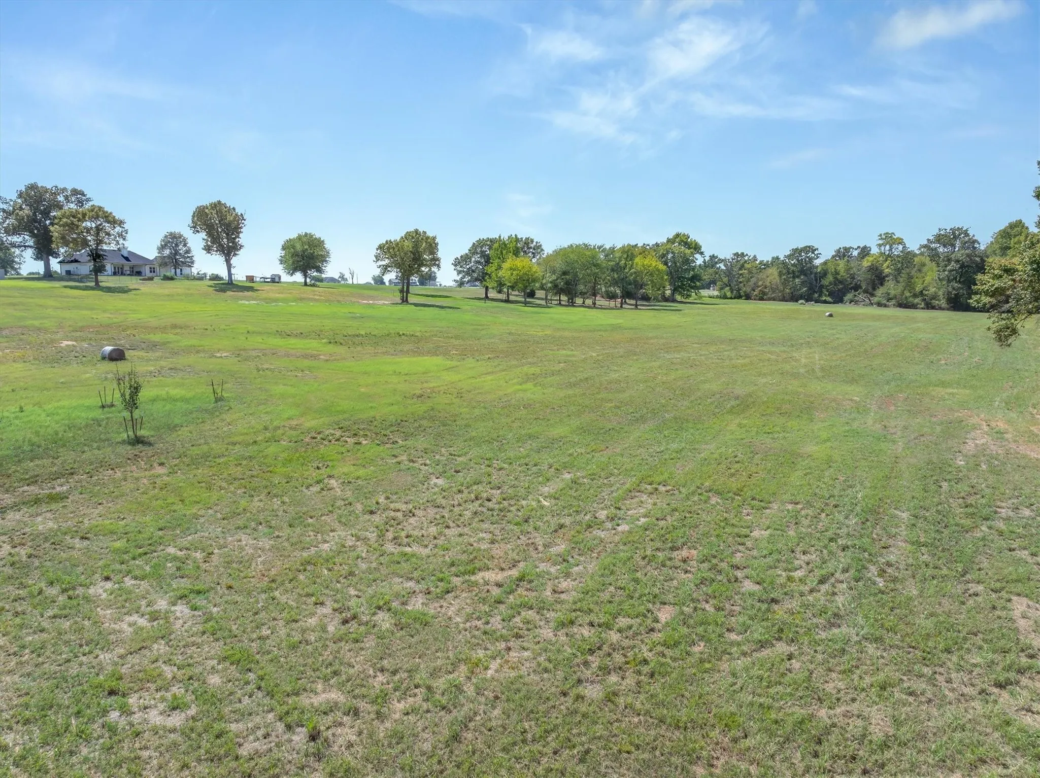 Expansive green acreage featuring a distant residence and mature trees