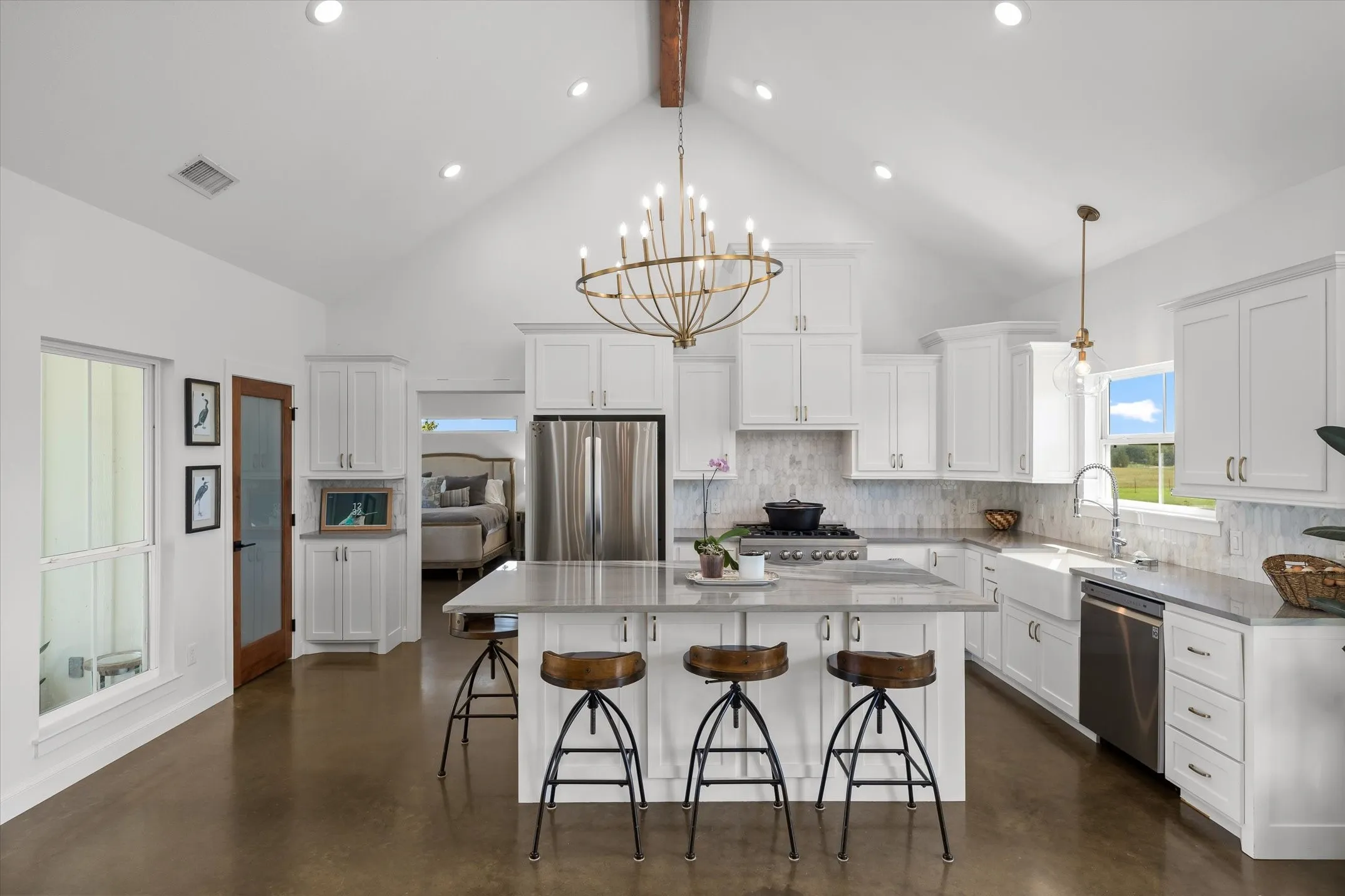 Vaulted ceiling with exposed wood beam, white cabinetry, integrated stainless steel appliances, stone-finish countertops, and wood-finish flooring