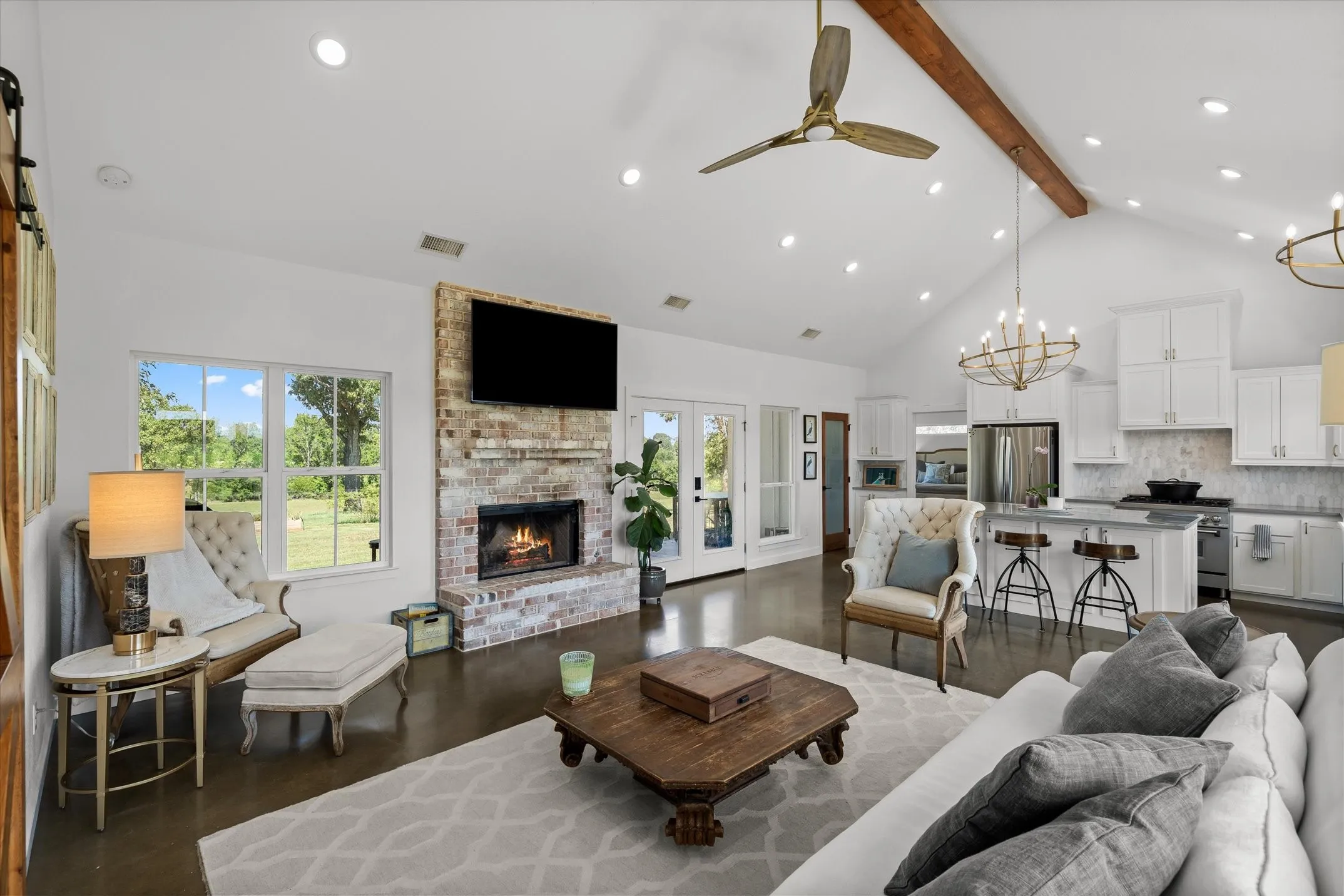 Vaulted ceiling with exposed wood beam, brick fireplace, wood-finish flooring, white cabinetry, and stainless steel appliances