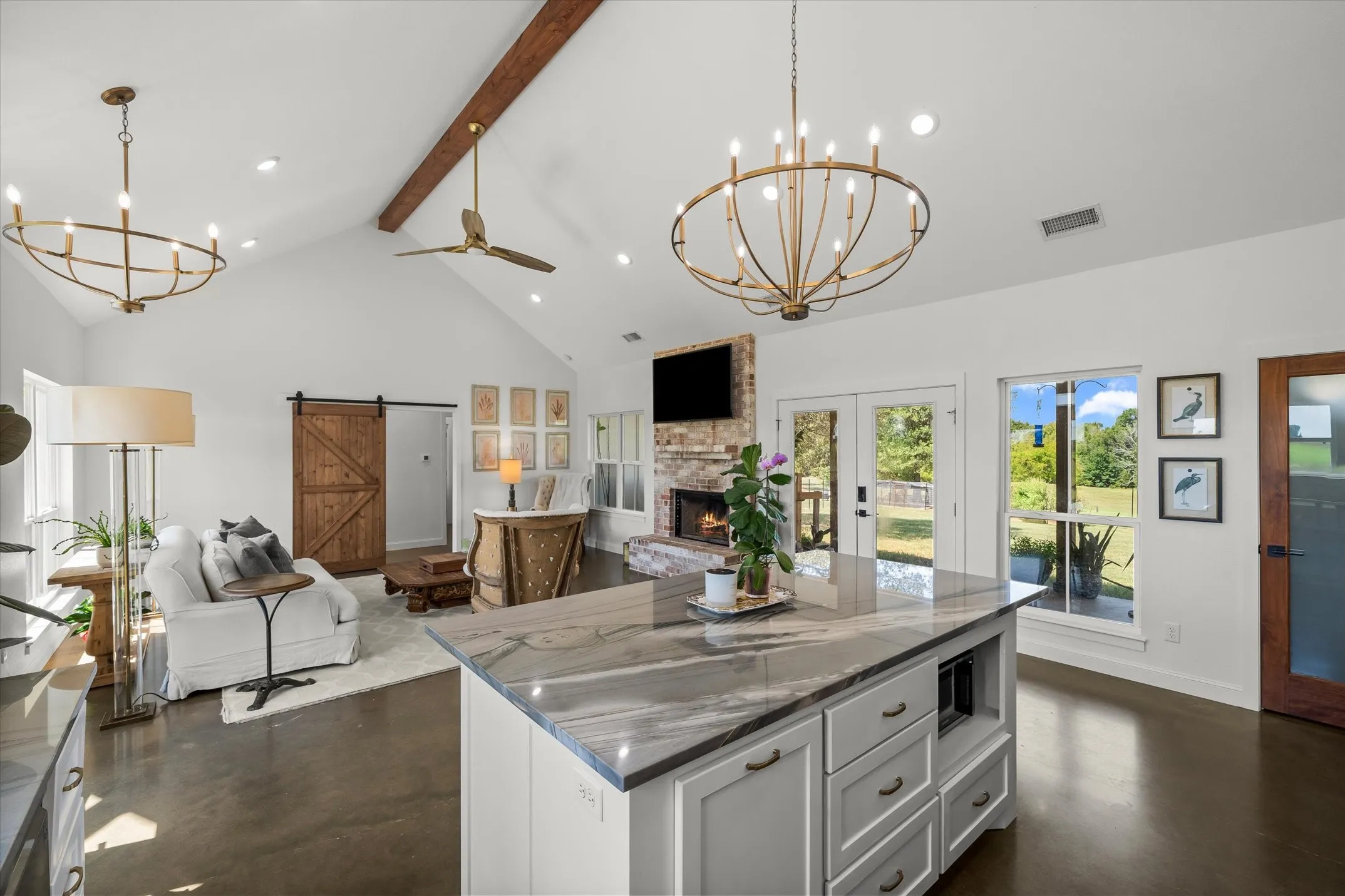 Vaulted ceiling with exposed wood beam, a stone-clad fireplace, and a kitchen island featuring a stone countertop