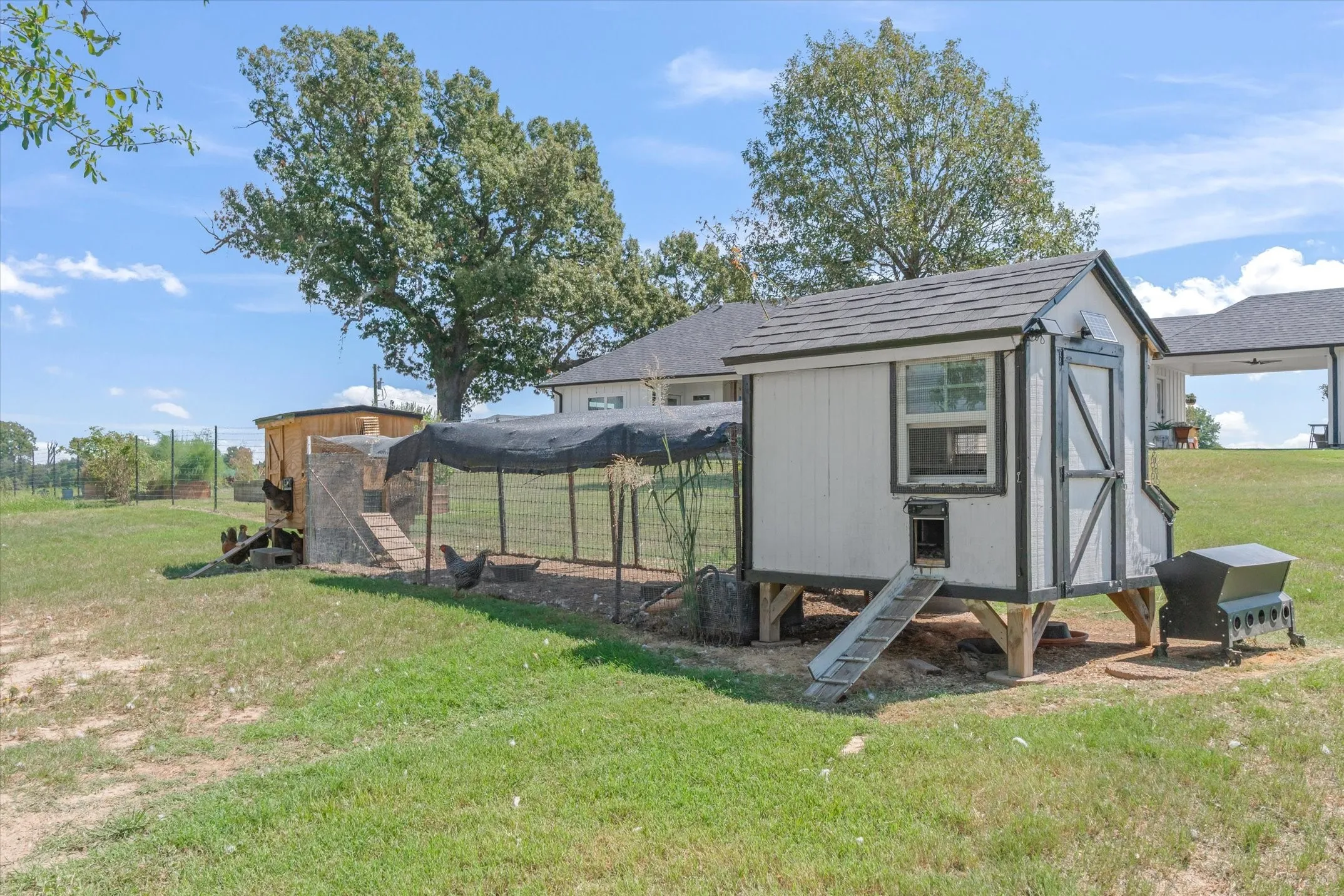 Well-maintained chicken coop with shingled roof, attached run, and fenced enclosure