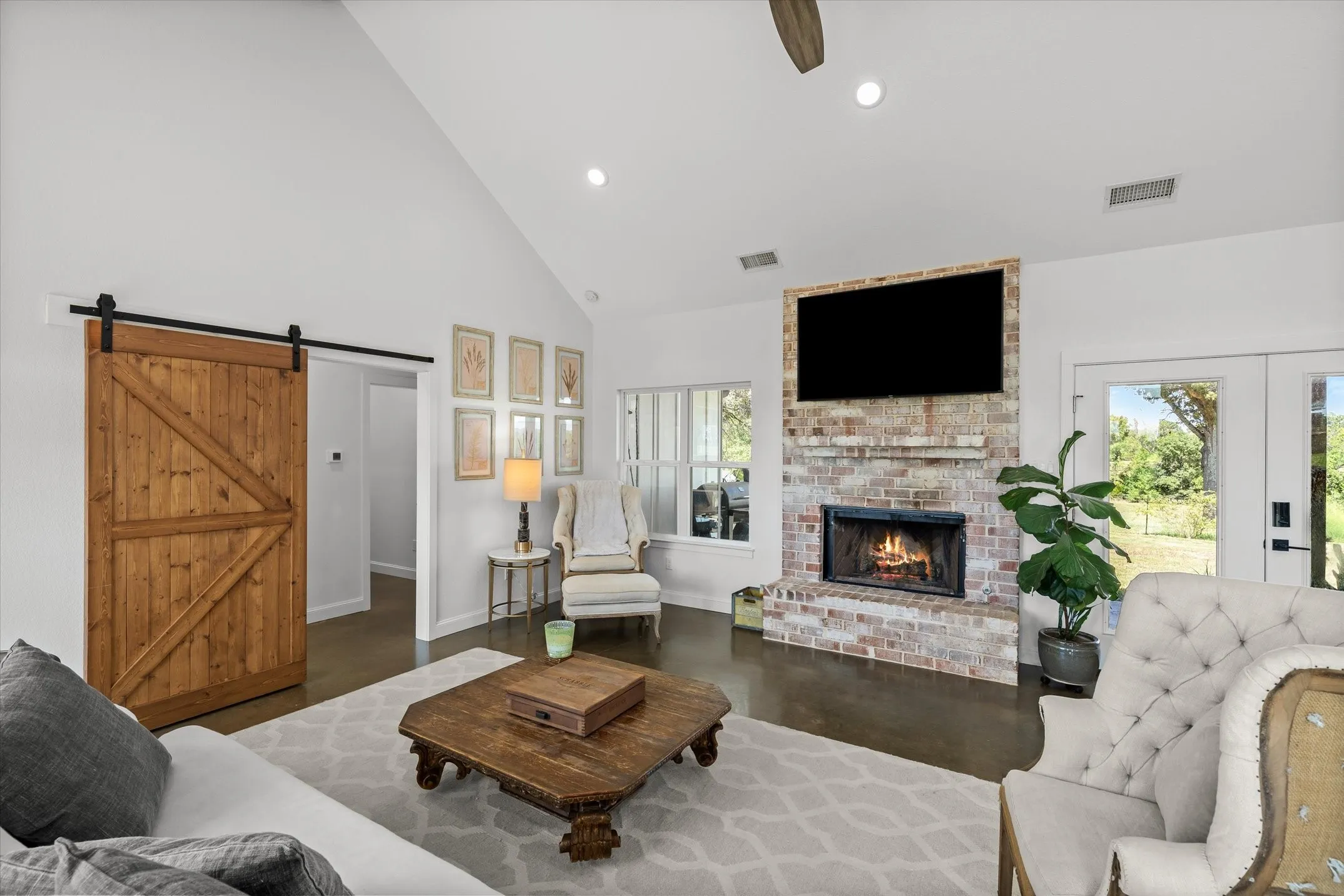 Vaulted ceiling with recessed lighting, brick fireplace with mounted media, wood-finish flooring, and a sliding barn door