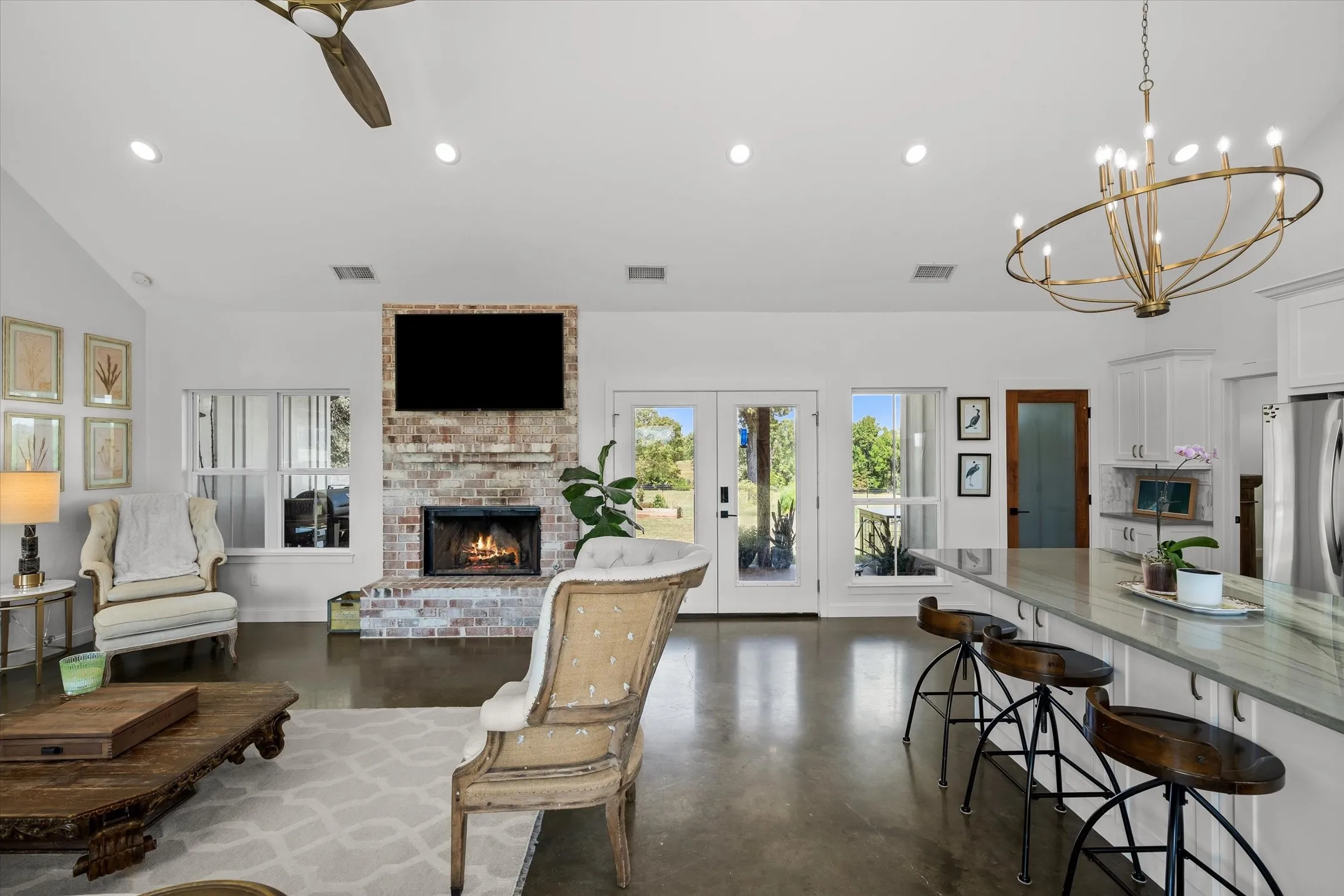 Vaulted ceiling with recessed lighting, brick-faced fireplace, French doors, extensive kitchen island with countertop, and overhead chandelier