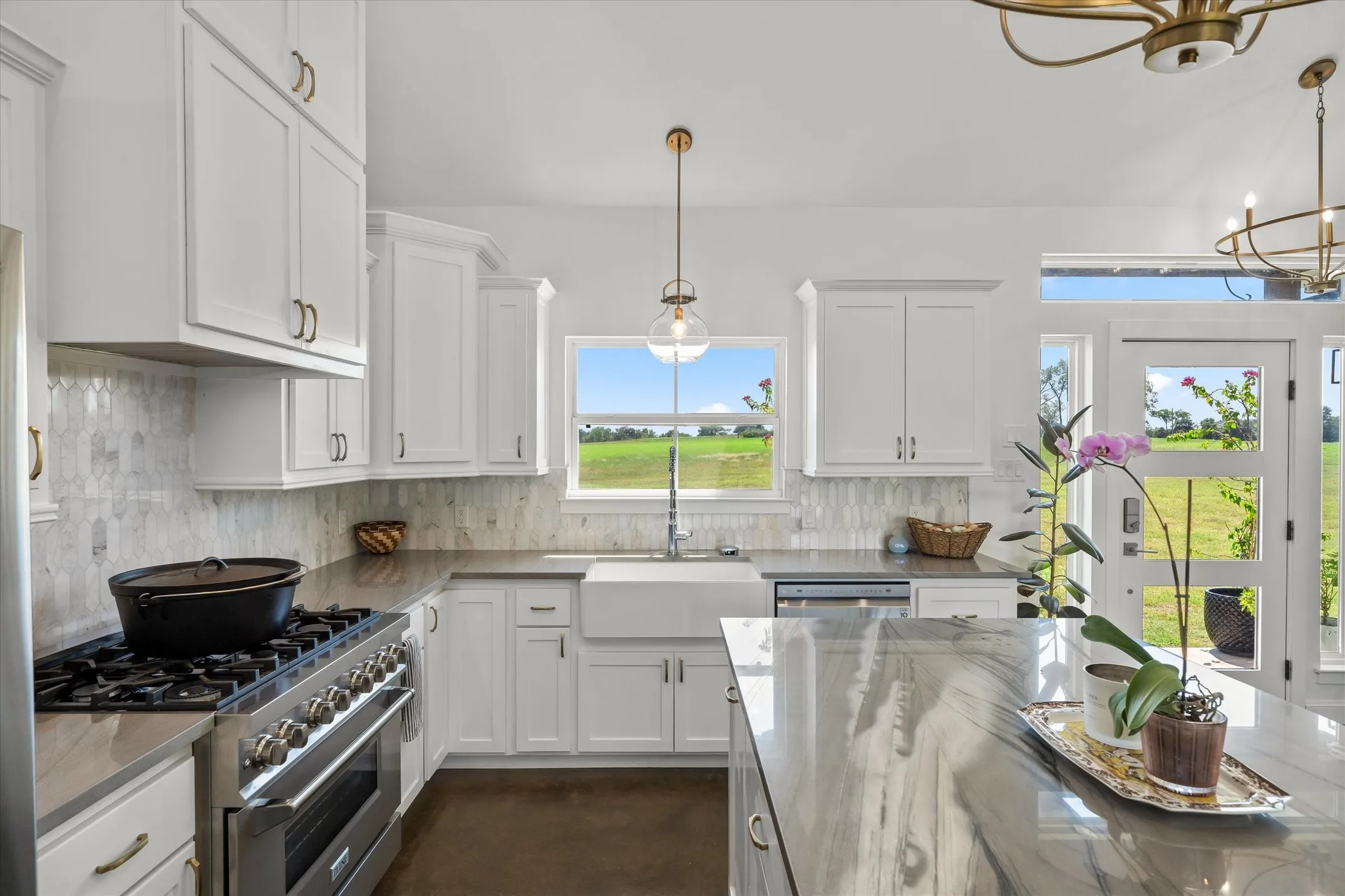 White cabinetry with brass hardware, stainless steel range, farmhouse sink, stone countertops, and a full-light entry door