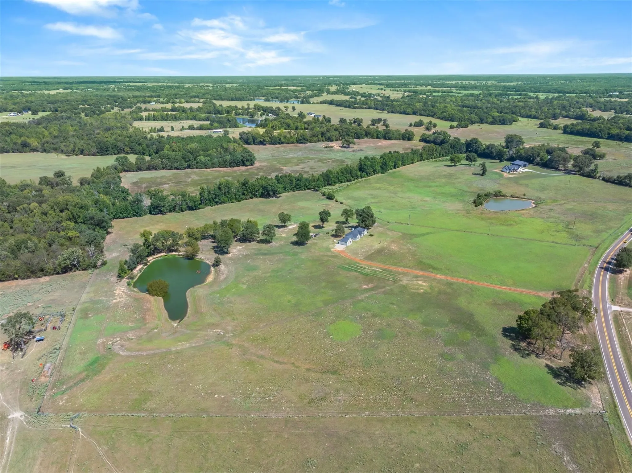 Expansive green acreage featuring multiple ponds, scattered trees, and a distant road