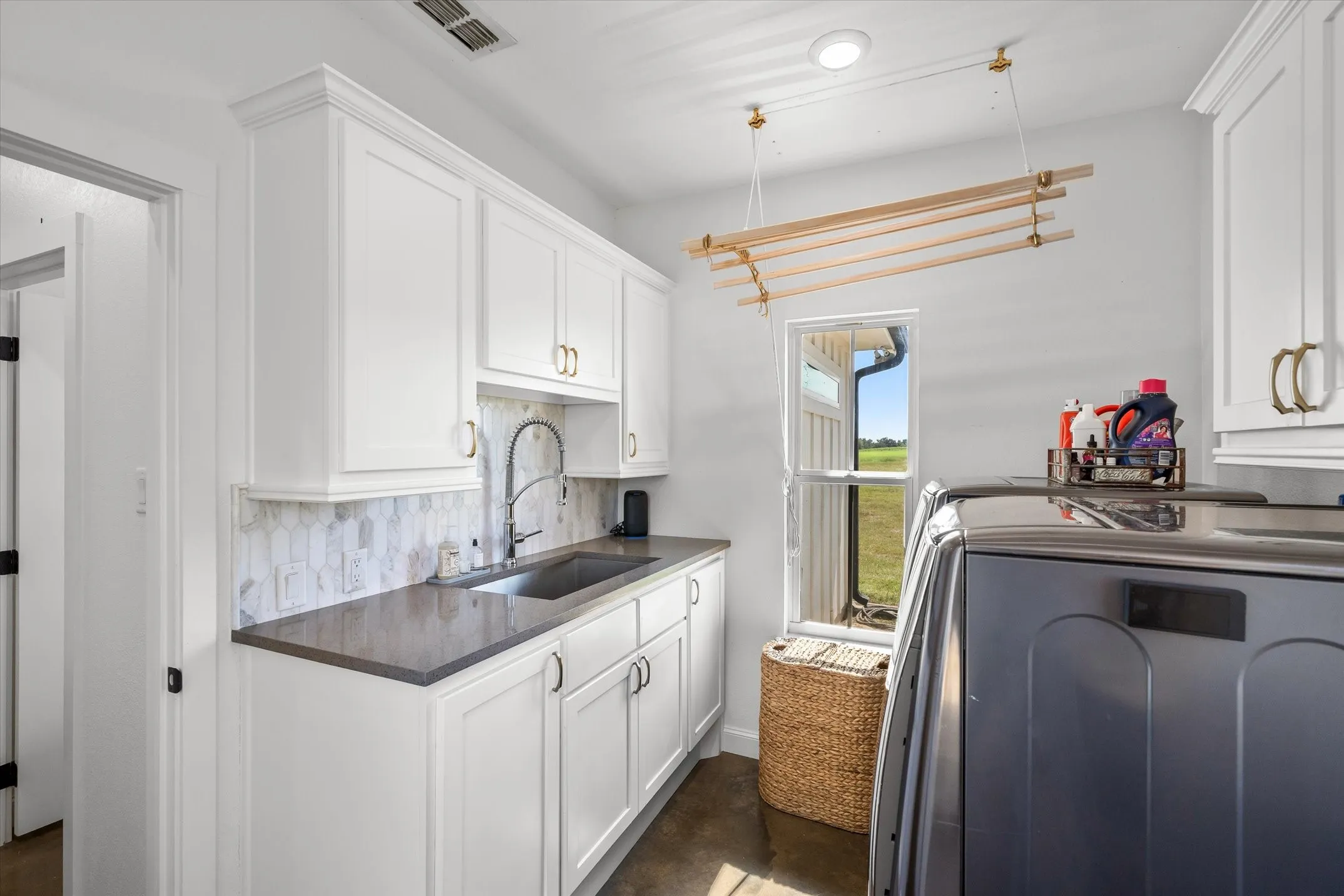 White shaker-style cabinetry with gold-tone hardware, dark countertop, under-mount sink with gooseneck faucet, and a patterned tile backsplash