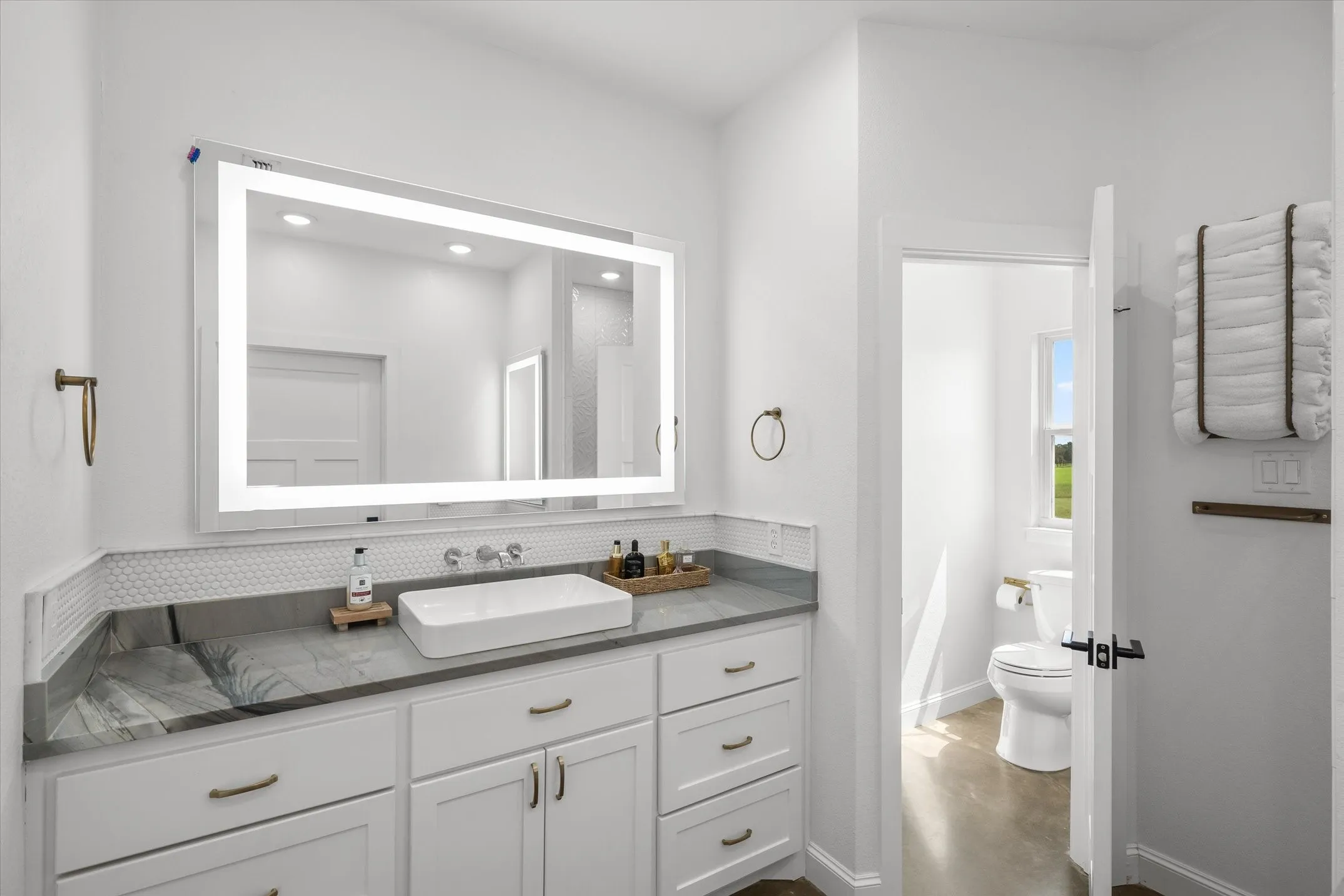 Vanity with rectangular vessel sink, stone countertop, honeycomb tile backsplash, and an illuminated mirror