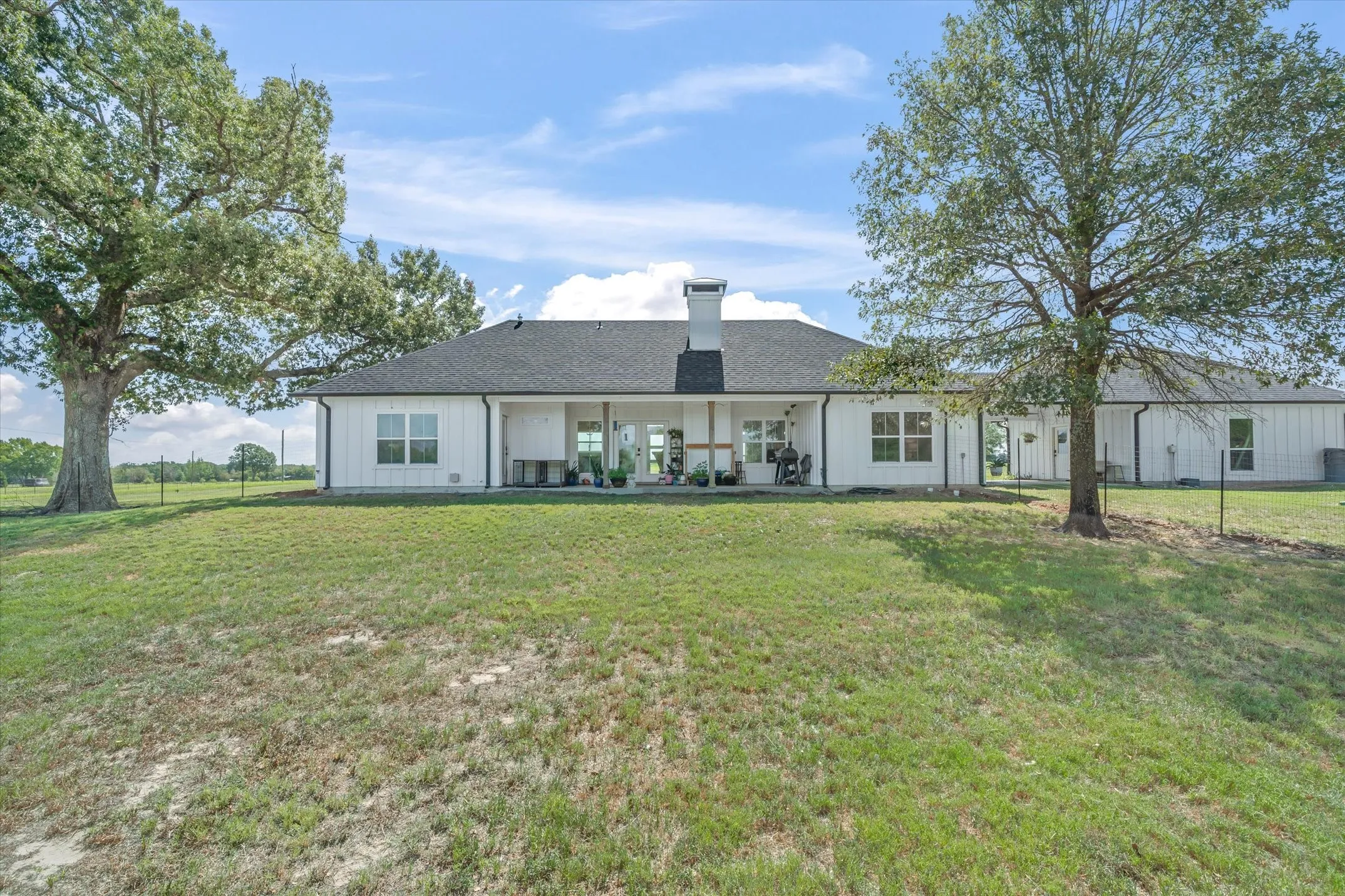Expansive rear elevation featuring white board-and-batten siding, a covered patio, and a dark shingled roof