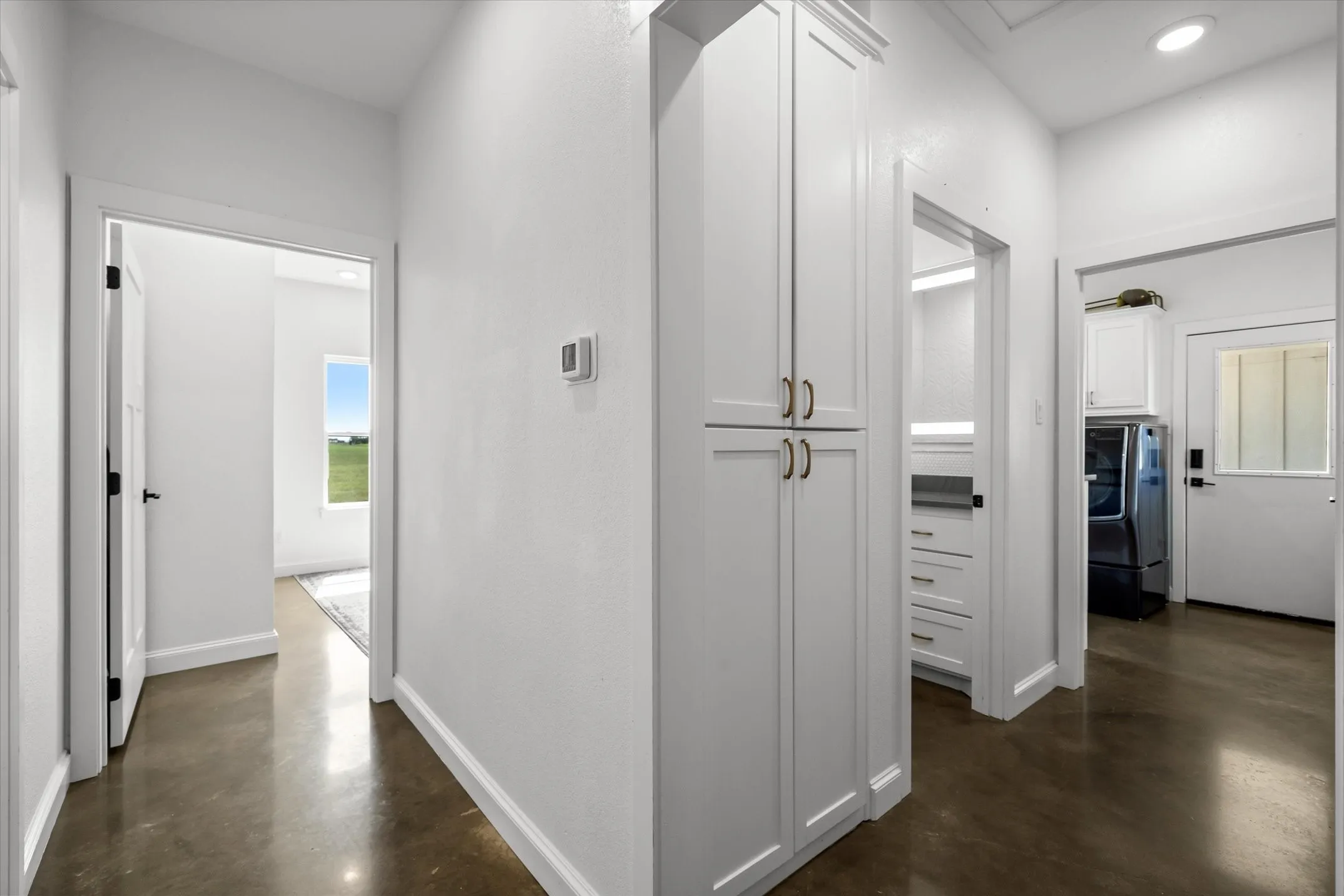 White cabinetry with brass hardware, polished concrete flooring, white interior doors with black hardware, recessed lighting, and a window with exterior scenery