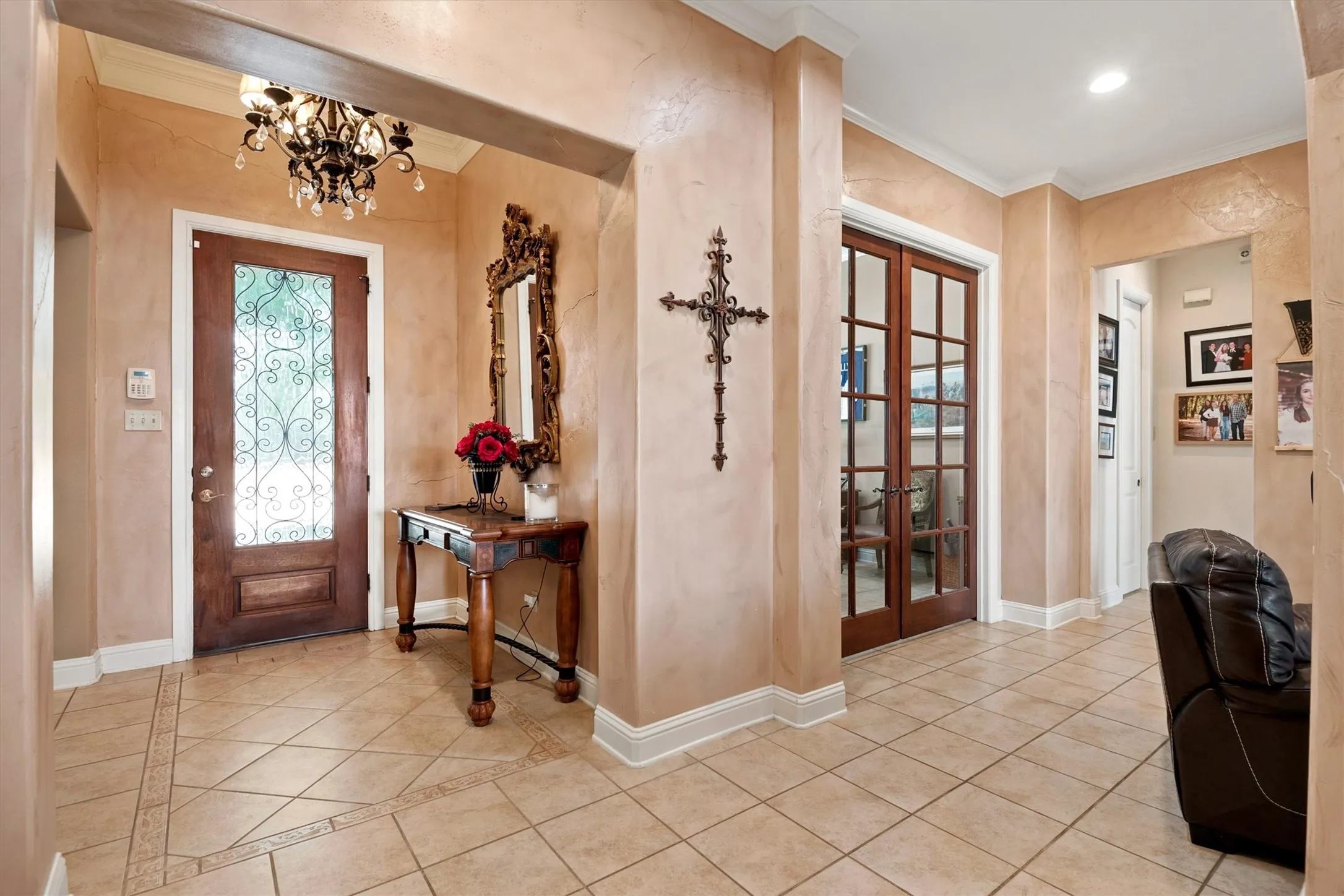 Tiled flooring featuring a decorative border, a prominent chandelier, a wooden entry door with decorative glass, and interior French doors