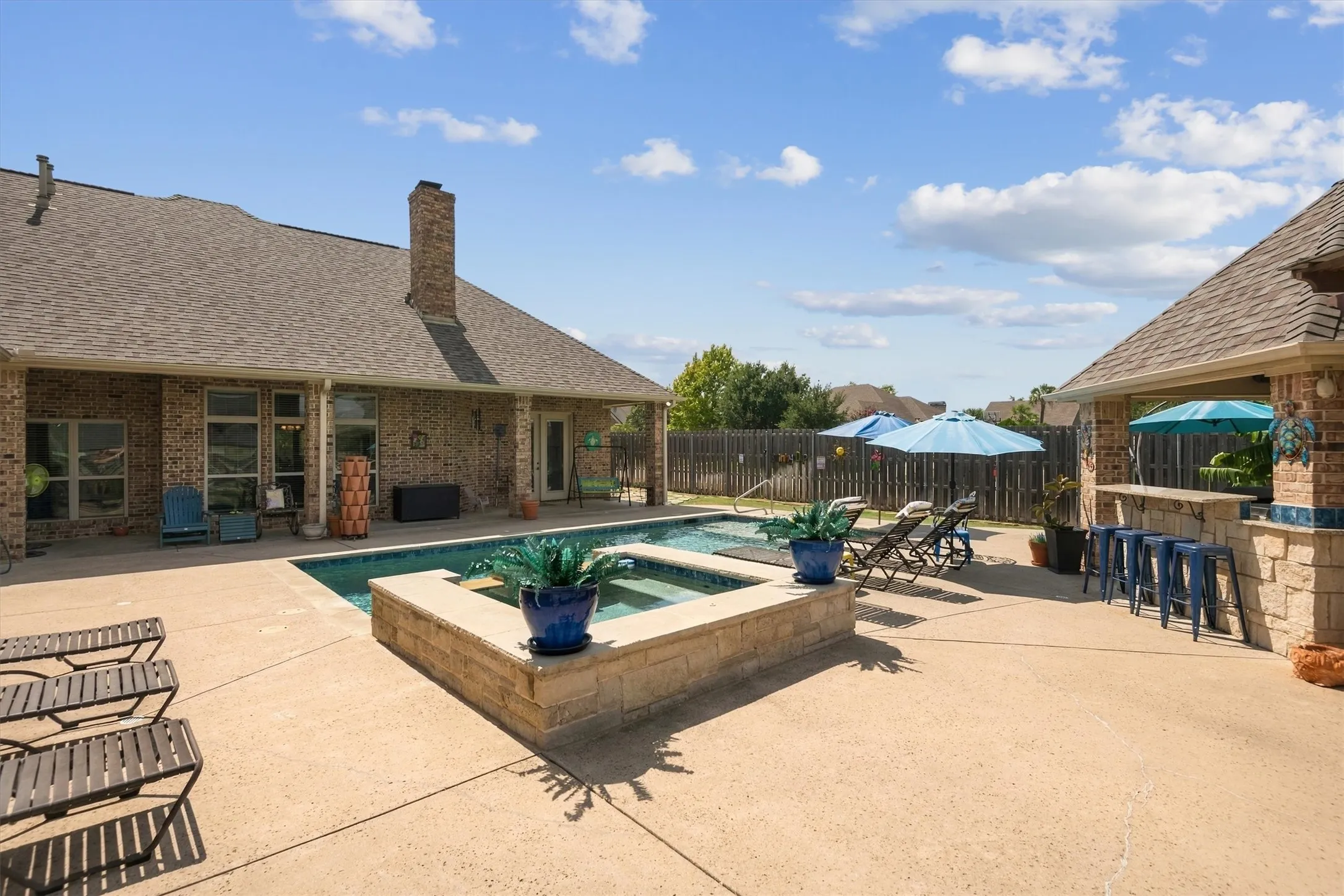 Concrete patio featuring an in-ground swimming pool, a raised spa, and a built-in outdoor kitchen with stone veneer