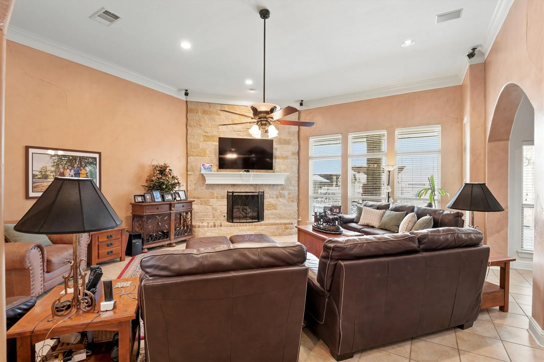 Living area featuring a stone accent wall fireplace, arched doorway, recessed lighting, and crown molding