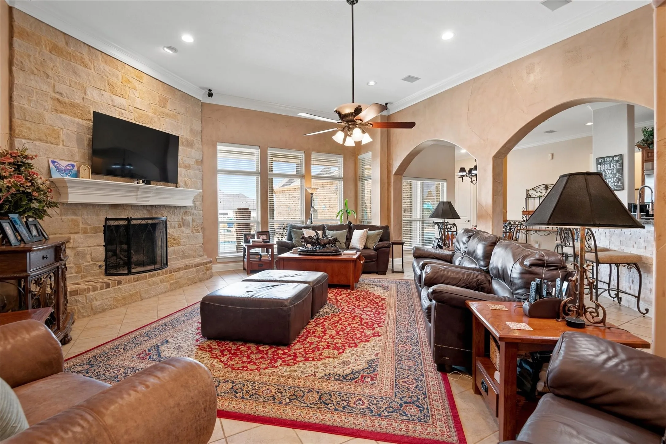 Stone fireplace with a white mantel, recessed lighting, arched doorways, tiled flooring, and a ceiling fan